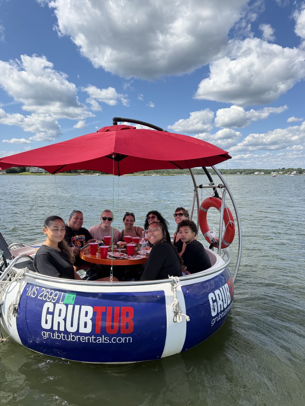 A group under the red umbrella on a GrubTub in Padanaram Harbor